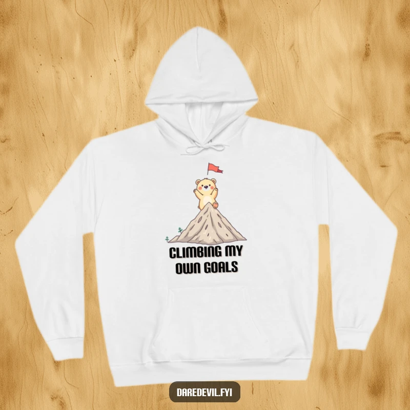 Funny bear hoodie showing a whimsical bear triumphantly planting a flag on a tiny mountain peak, ready to celebrate.